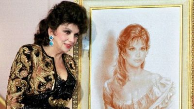 Фото. Итальянская актриса Джина Лоллобриджида рядом со своей фотографией в молодости на телевизионном аукционе 19 октября 1999 года в Каире. Фотография была продана за $5тыс, а платье — за $2 тыс. (AMR NABIL/AFP via Getty Images)