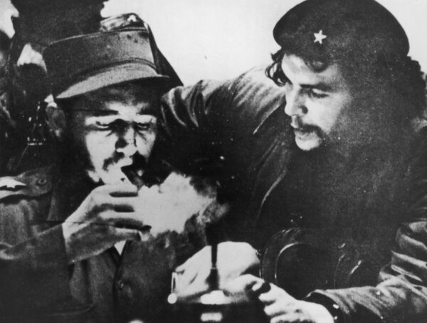 Кубинский революционер Фидель Кастро (слева) закуривает сигару, а аргентинский революционер Че Гевара наблюдает за первыми днями их партизанской кампании в горах Сьерра-Маэстра на Кубе, около 1956 года. (Hulton Archive/Getty Images)