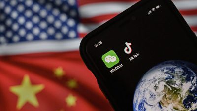 На этой фотоиллюстрации можно увидеть мобильный телефон с логотипами китайских приложений WeChat и TikTok перед монитором с флагами США и Китая на интернет-странице. (Kevin Frayer/Getty Images)
