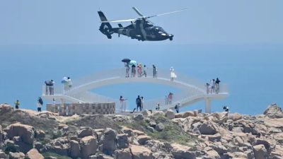 Туристы наблюдают, как китайский военный вертолёт пролетает мимо острова Пинтань, одного из ближайших пунктов материкового Китая к Тайваню, в провинции Фуцзянь, 4 августа 2022 года. (Hector Retamal/AFP via Getty Images)