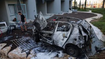 Мужчина идёт рядом с автомобилем, уничтоженным в результате ракетного обстрела из сектора Газа в южном израильском городе Ашкелон 10 октября 2023 года. (Jack Guez/AFP via Getty Images)