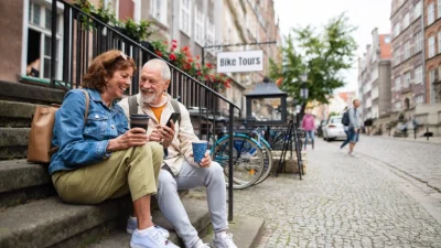Счастливая пожилая пара туристов сидит на лестнице и пьёт кофе. (Halfpoint/Shutterstock)
