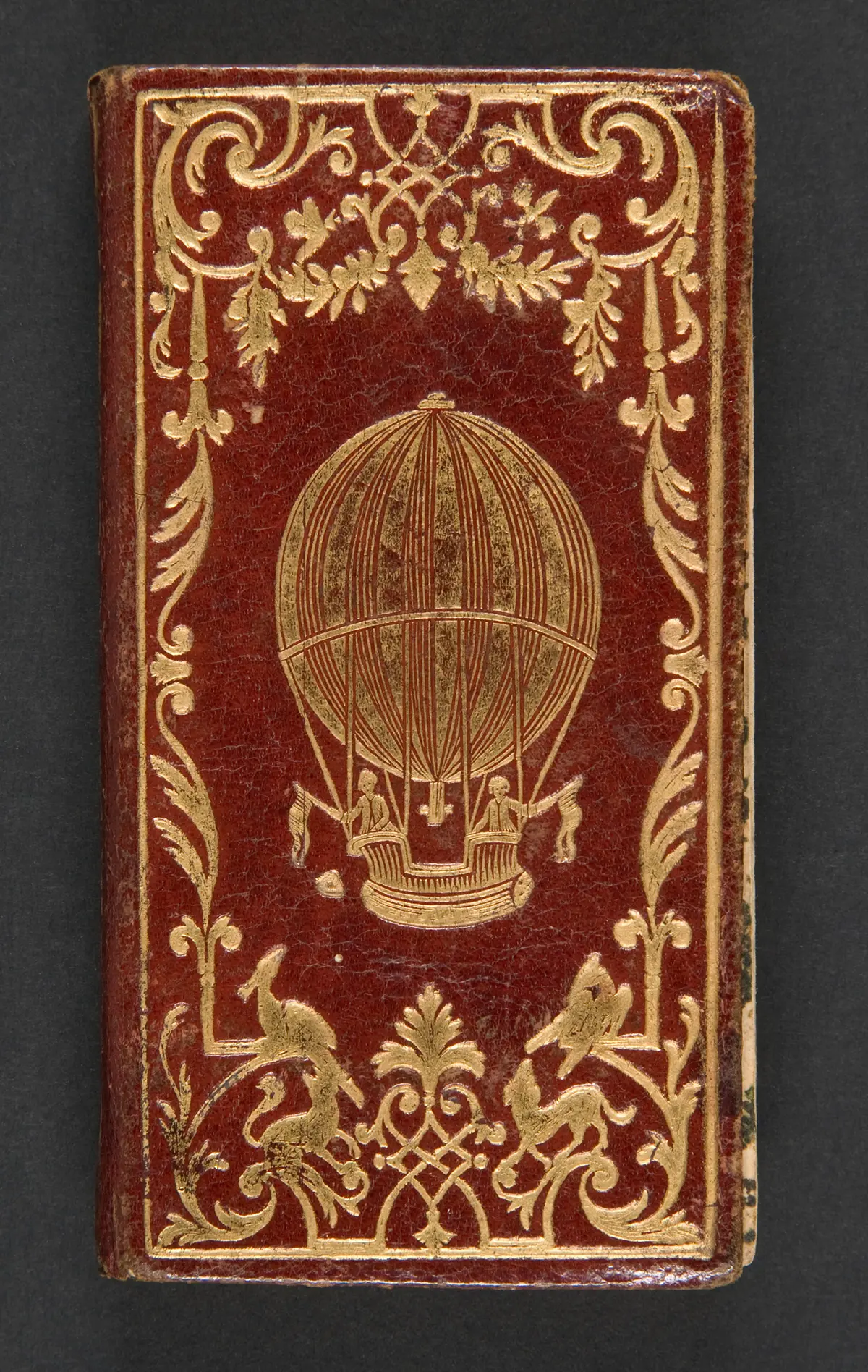 Передняя обложка книги «Le Calendrier de la Cour», 1784 г., напечатанной в Chez La Veuve Hérissant и написанной Жаком Колломбатом. Современный красный марокко, искусная позолоченная рамка с золочёными шариками; 4 5/16 дюйма. Дар Джейна Райтсмана, Музей Метрополитен, Нью-Йорк. (Public Domain)