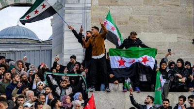 Сирийские беженцы в Турции размахивают флагами сирийской оппозиции, приветствуя падение режима Башара Асада. (YASIN AKGUL/AFP via Getty Images)