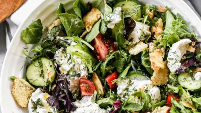 Ничто не имеет такого свежего вкуса, как этот салат «Буррата» с помидорами, огурцами, бурратой и свежей зеленью на подложке из смешанной зелени. Моя любимая часть — поджаренные чипсы из питы, посыпаемые сверху. (Lauren Allen)
