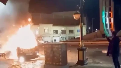 Кадр с иранского государственного телевидения показывает, как мужчина снимает на видео горящие автомобили во время ночных протестов в Зенджане, Иран, 9 января 2026 года. (Iranian state TV via AP)