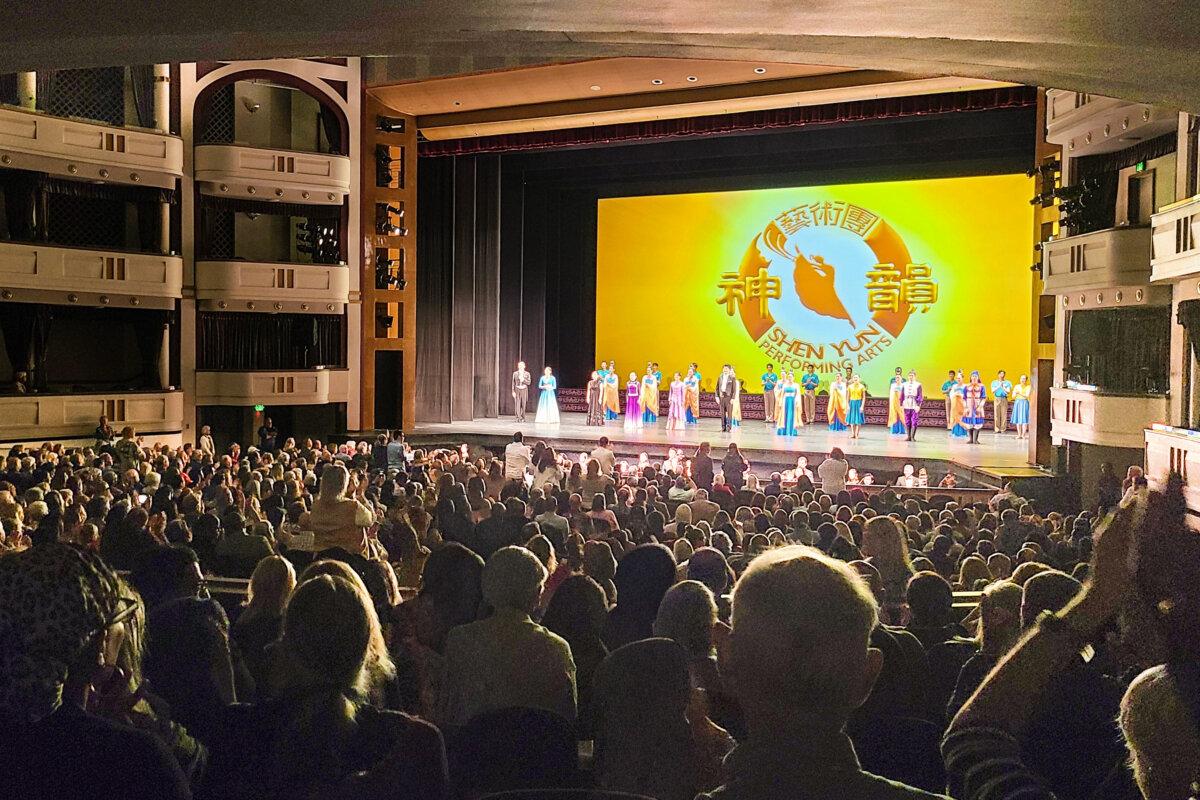 Заполненный зрительный зал и сцена с артистами труппы Shen Yun во время финальных поклонов.