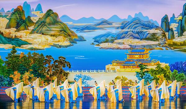 Артисты Shen Yun в голубых и белых костюмах исполняют танец со струящимися рукавами на фоне живописного китайского пейзажа.
