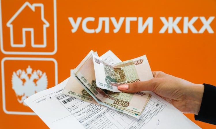 Рука держит квитанцию ​​по оплате услуг ЖКХ и российские рубли.