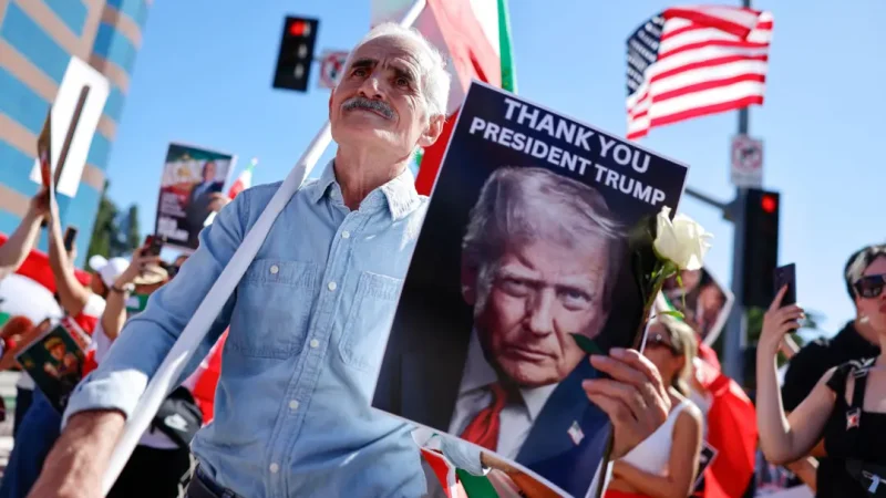 Мужчина на митинге иранской общины в США держит плакат с надписью Thank You President Trump на фоне американских флагов.