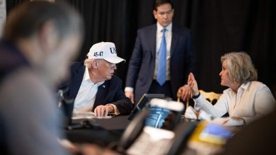 Дональд Трамп в белой кепке за столом совещаний следит за ходом военных действий.