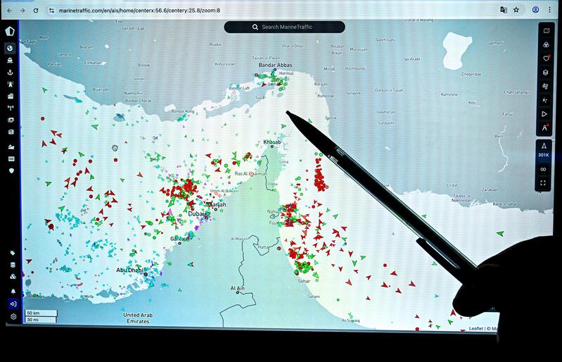 Рука указывает на интерактивную карту MarineTraffic, показывающую скопление судов в Ормузском проливе.