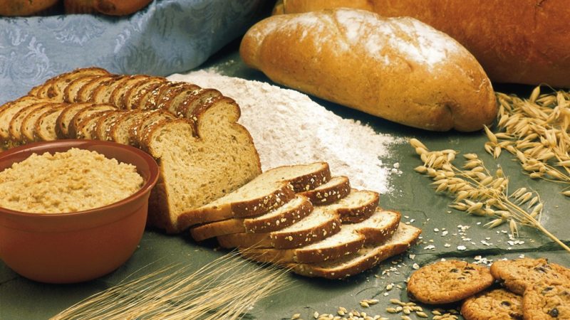 Ассортимент белого хлеба, выпечки, муки и колосьев пшеницы на столе.