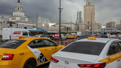 Жёлтые и белые автомобили такси в дорожном трафике на фоне Казанского вокзала и сталинской высотки в Москве.