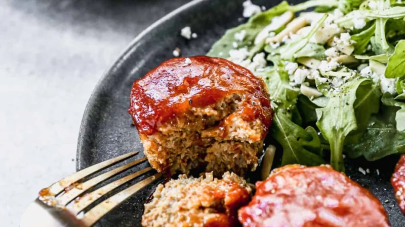 Рецепт мясных мини-рулетов Подача мясных мини-рулетов (маффинов) на темной тарелке с салатом из рукколы и сыром фета.