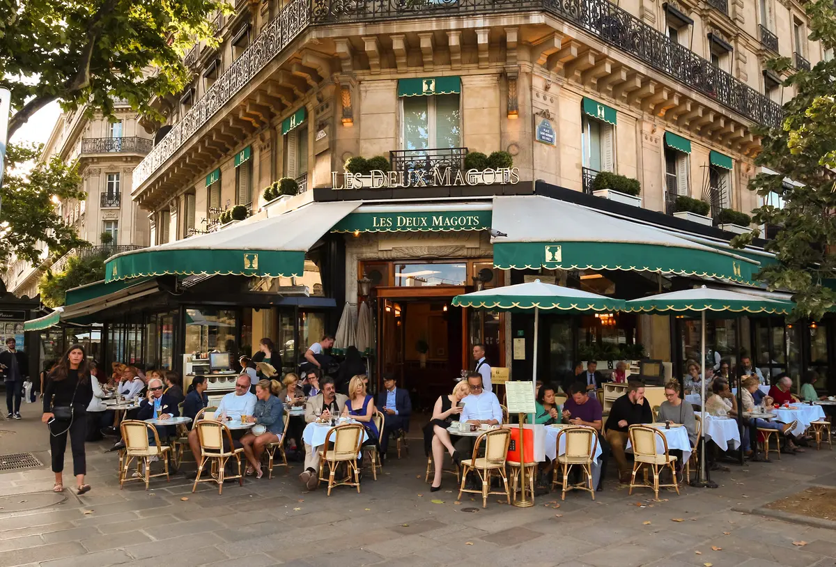 Посетители за столиками на террасе легендарного кафе Les Deux Magots в Париже.