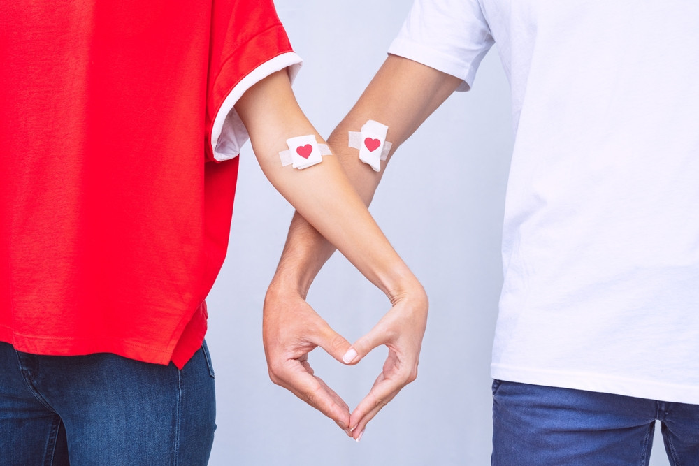 Пара с пластырями на руках после сдачи крови сложила руки сердечком