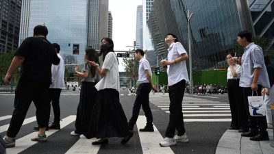 Молодые люди в деловых костюмах переходят дорогу на фоне небоскрёбов в центральном деловом районе Пекина.