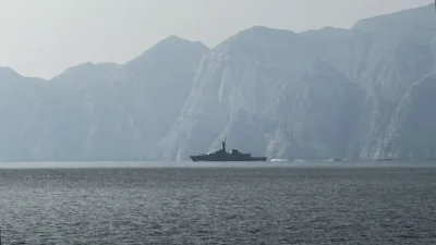 Силуэт военного корабля в тумане на фоне скалистых берегов Ормузского пролива в Иране во время начала военного конфликта 2026 года.