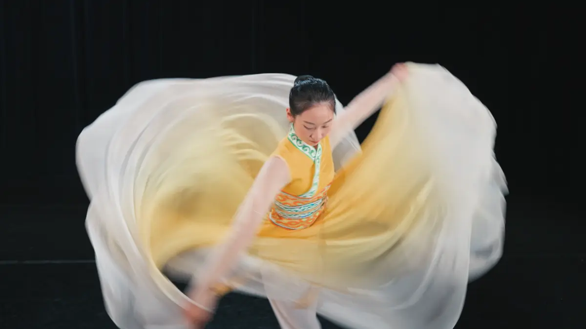 Танцовщица Shen Yun в желтом платье выполняет вращение