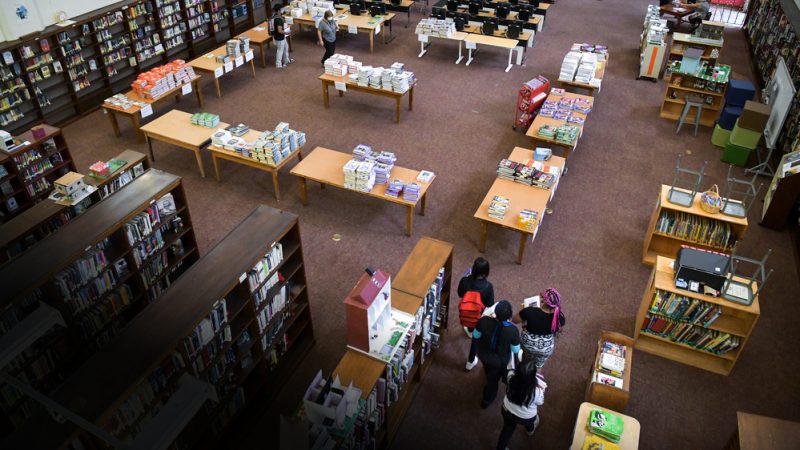 Школьники выбирают книги в библиотеке среди стеллажей и столов
